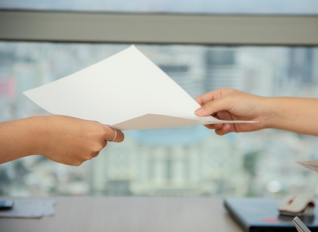 Two people exchanging documents across a wooden desk.